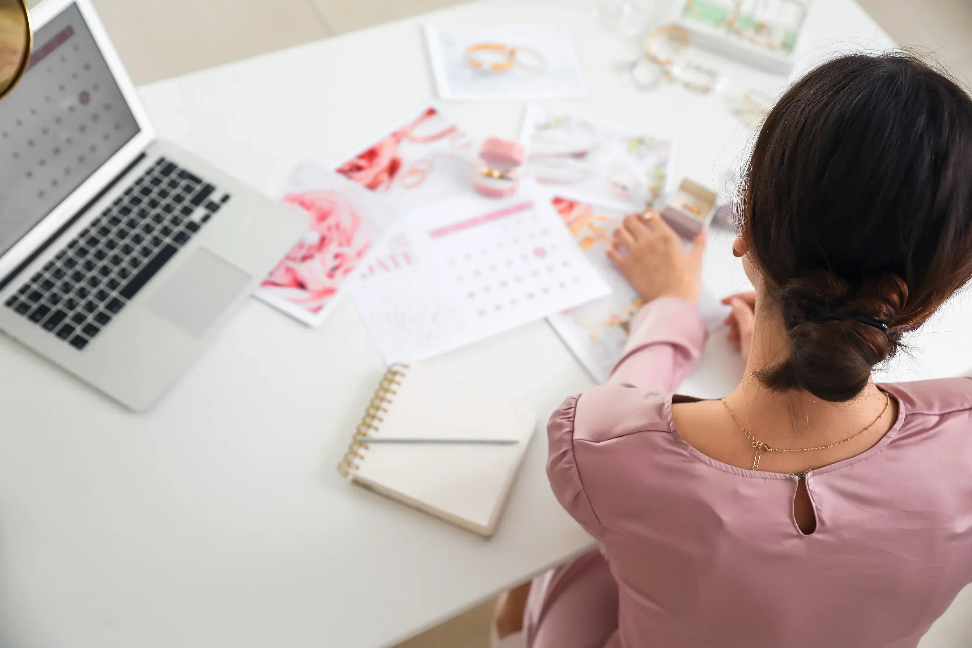 Female wedding planner organizing rings and calendar at office desk with laptop and notebook