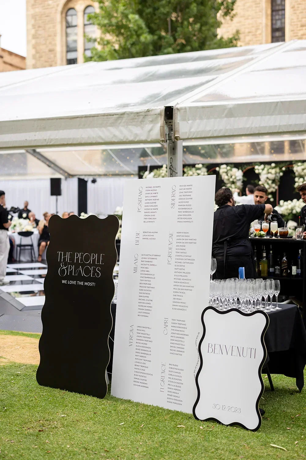 Wedding reception seating chart with The People and Places sign and Benvenuti welcome at outdoor marquee