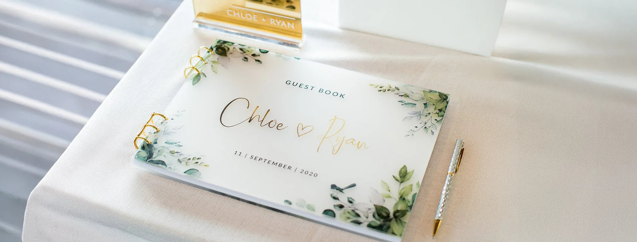 A custom wedding guest book with a frosted acrylic cover, decorated with a watercolour eucalyptus design and the couple's names in gold foil script.