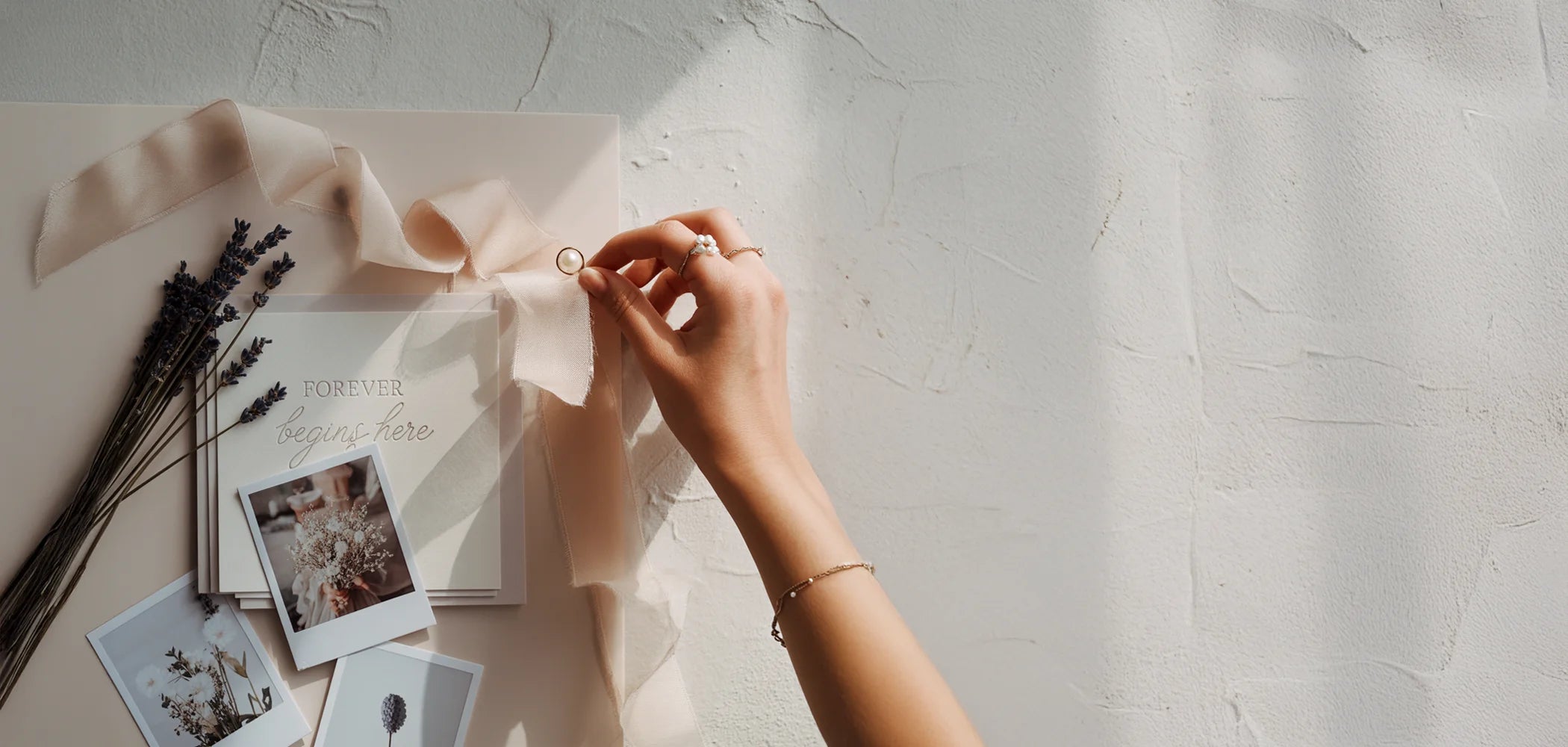 Elegant hands holding a pearl over luxury wedding stationery, illustrating the simple, bespoke invitation design process at Felicitations.