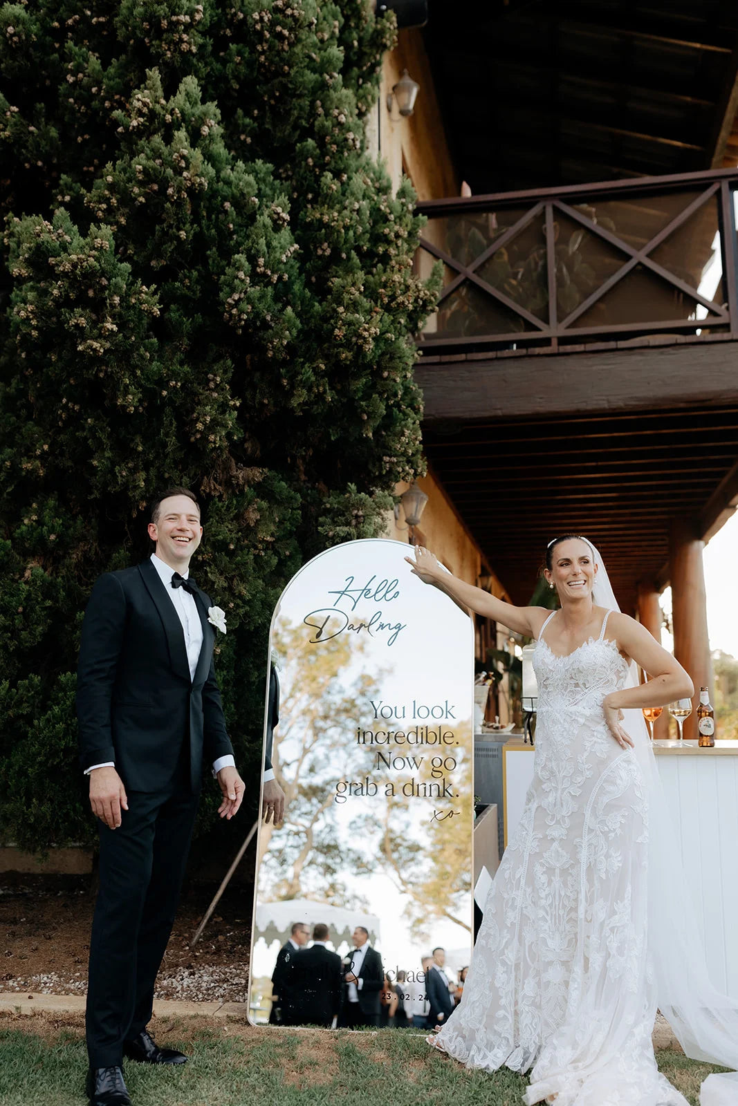 A wedding couple standing next to a decorative mirror sign outdoors.