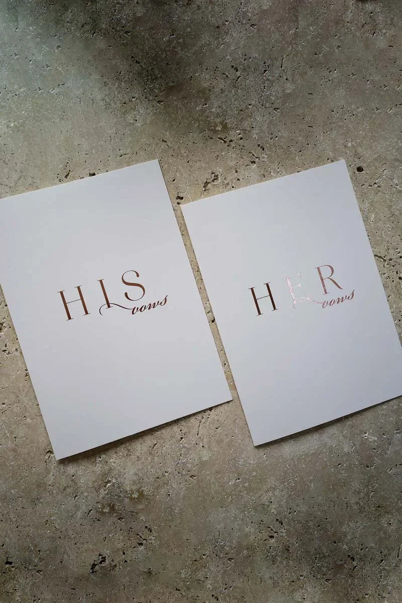 Minimalist HIS and HER wedding vow booklets with elegant rose gold foil text on grey stone background