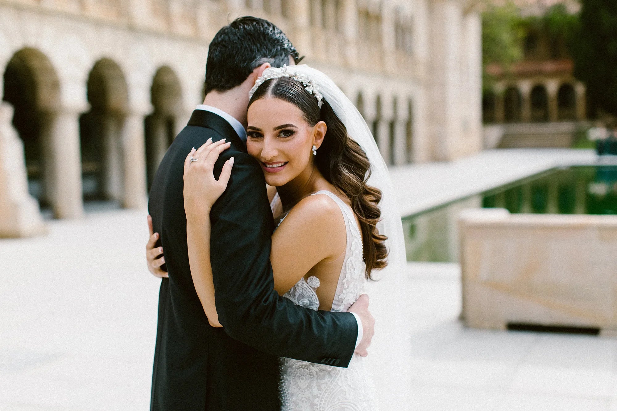 A beautiful bride smiling happily as she embraces her groom on their wedding day at a classic Perth venue with stone arches.