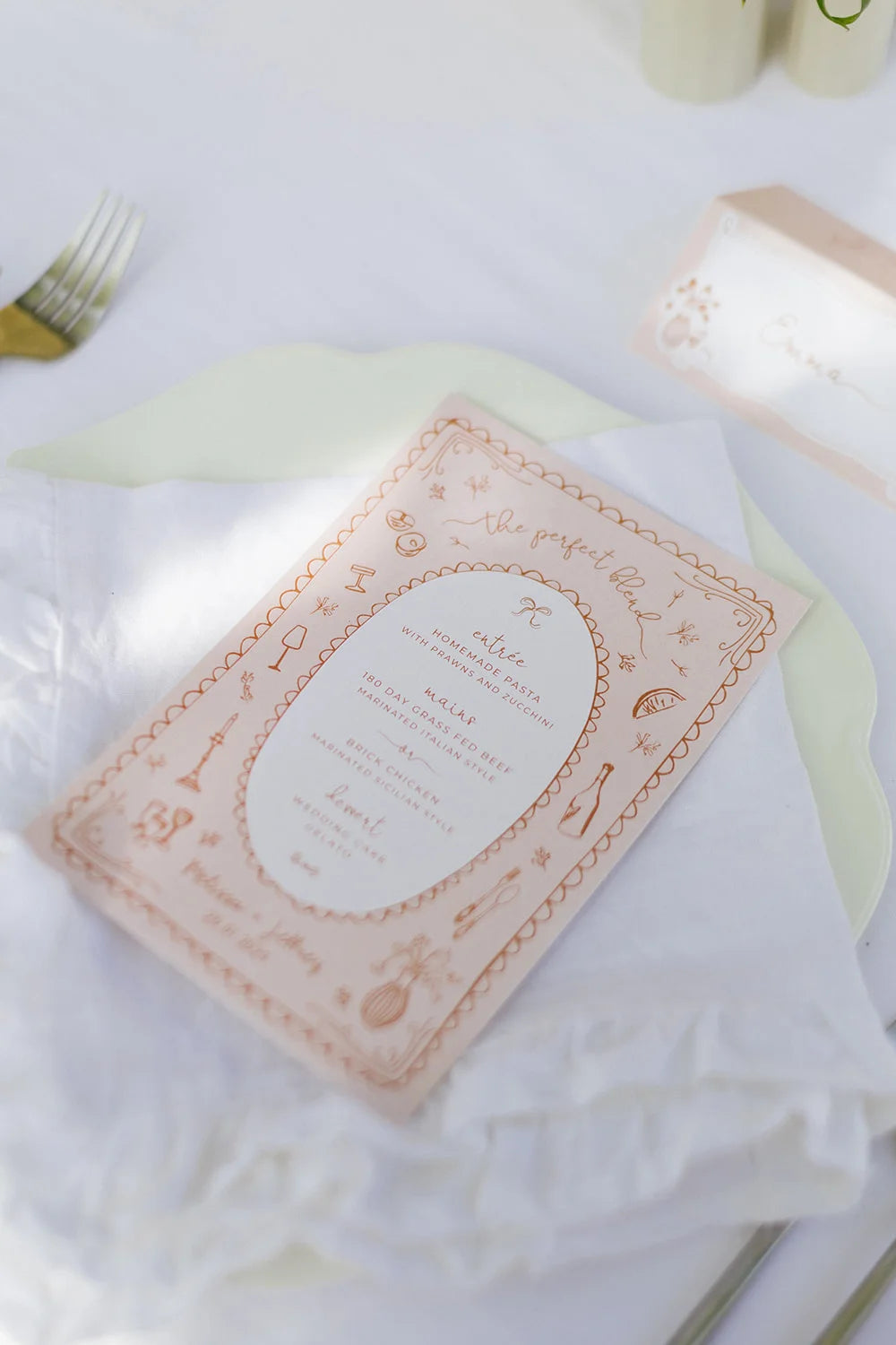 A custom wedding menu card in a terracotta pink colour, featuring a border of charming, hand-drawn illustrations of food and drinks.