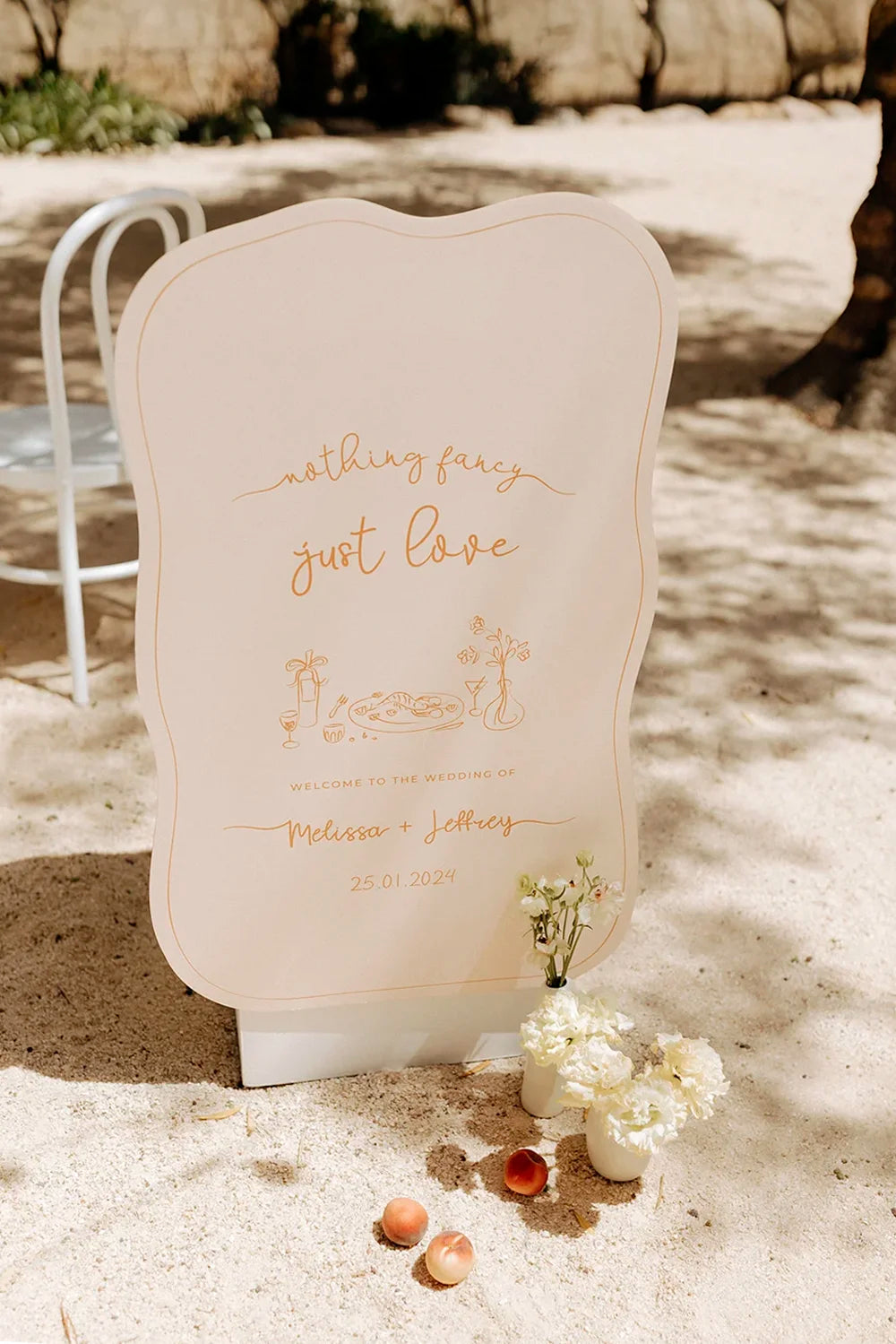 A modern wedding welcome sign in a custom organic die-cut shape, featuring the quote 'nothing fancy just love' in elegant script.