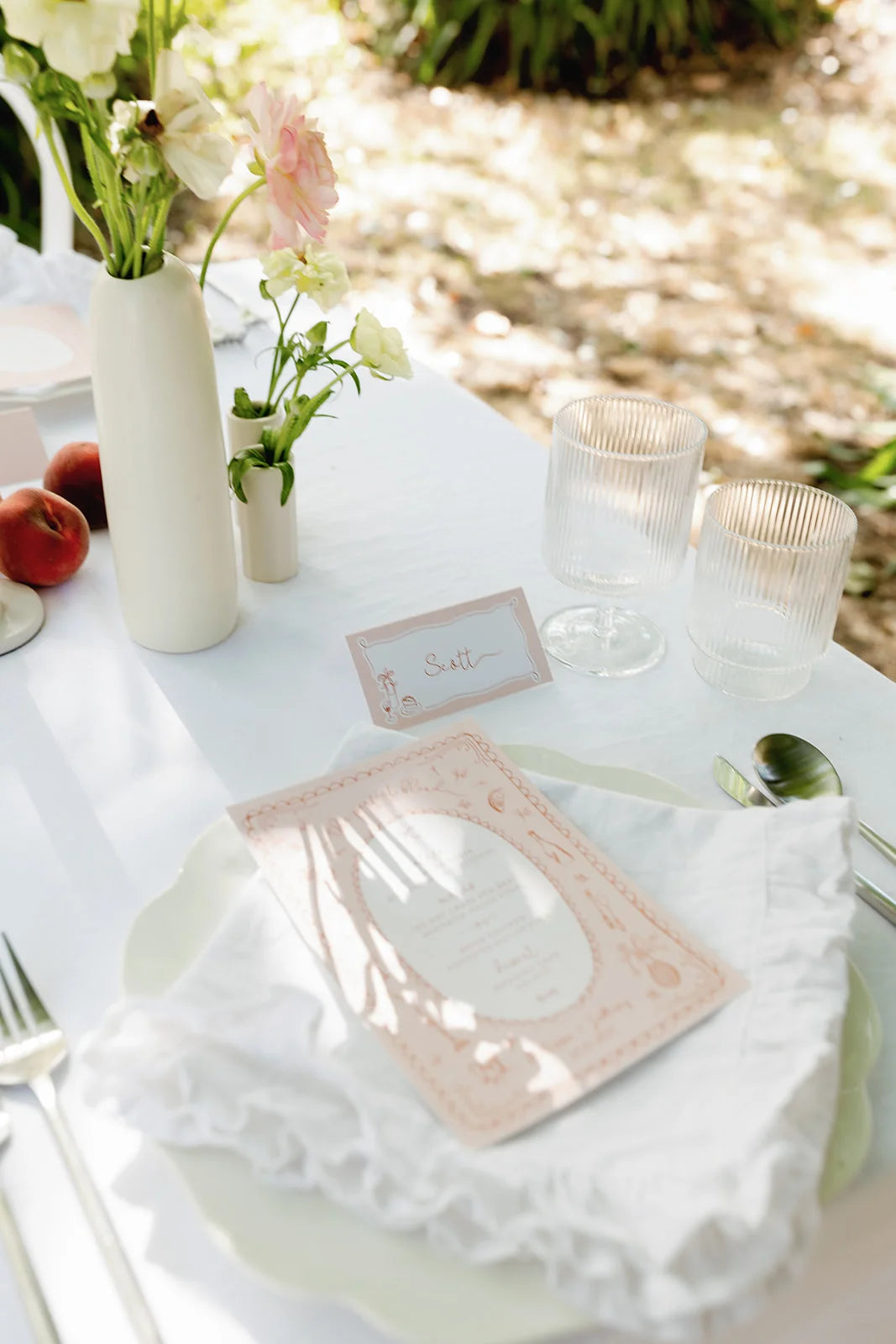 Custom-illustrated blush pink wedding menu and matching place card for Scott at outdoor reception with peaches and floral vase