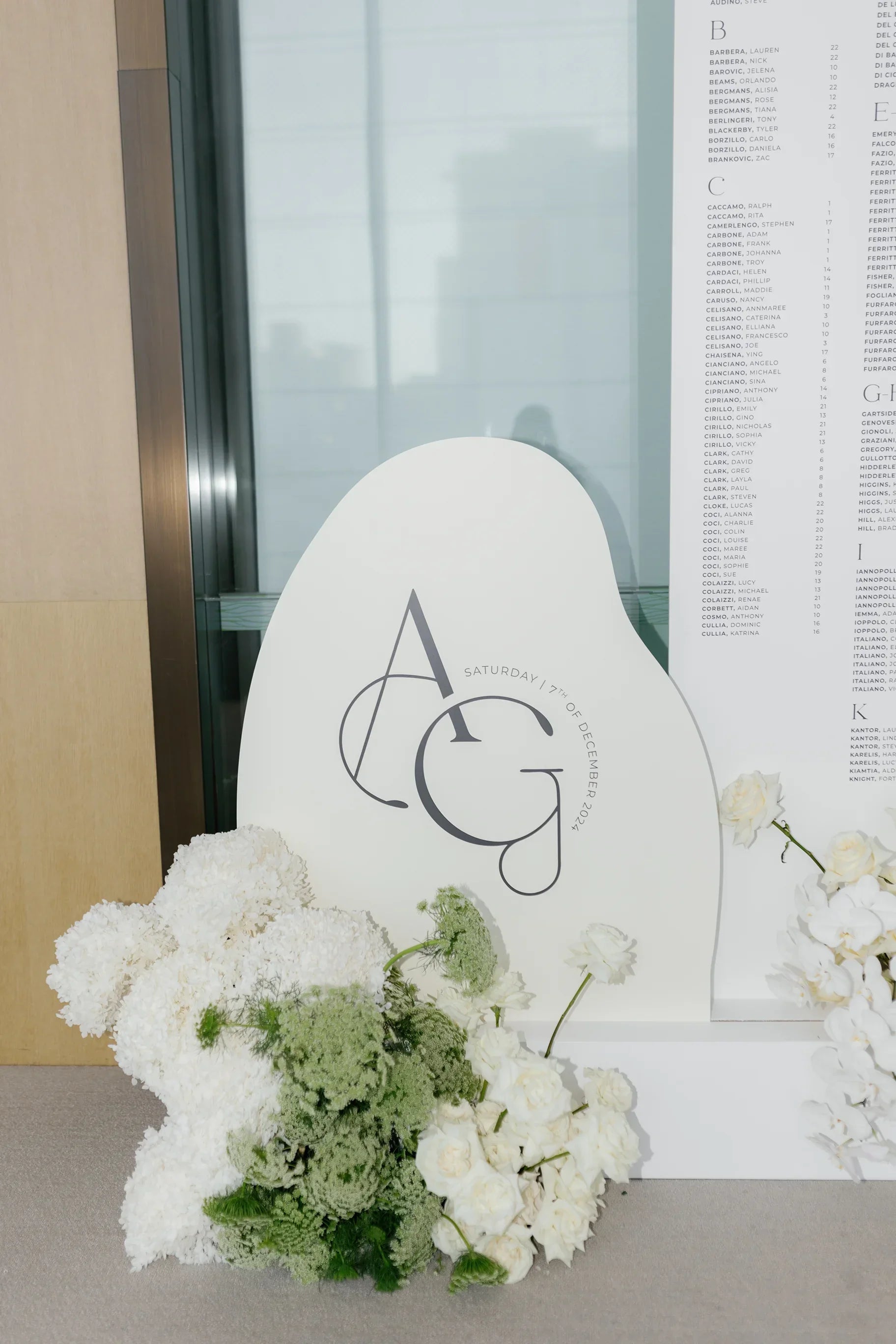 Custom-shaped white wedding welcome sign with initials AG and floral arrangements