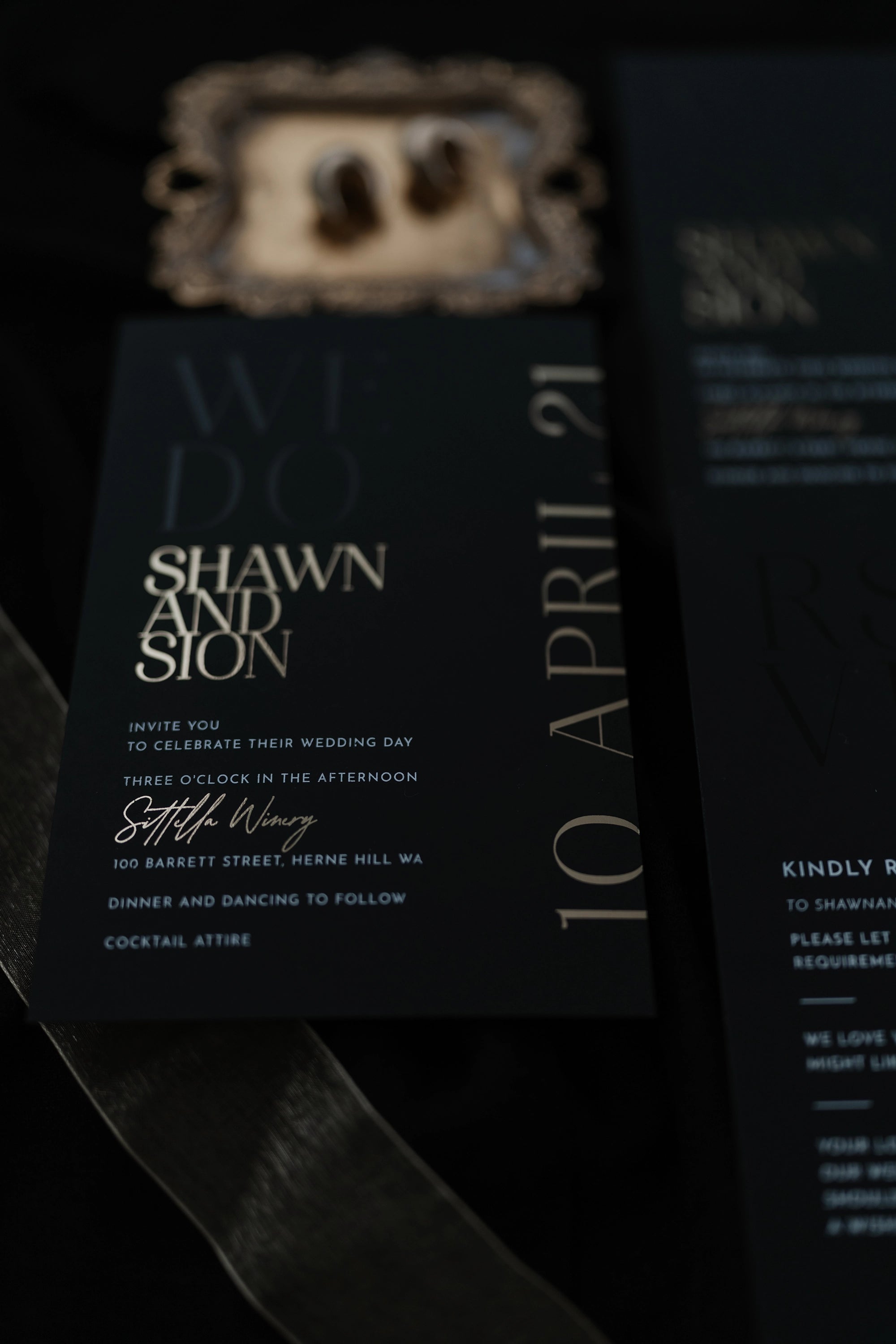 The Monaco suite close-up — moody black invitation with rose gold foil names Shawn and Sion, side date 10 April 21, vintage frame in background