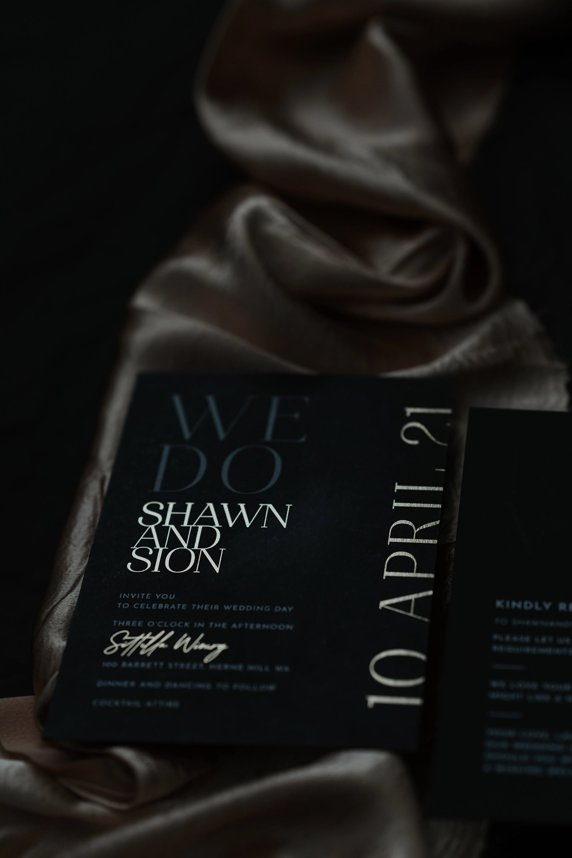 The Monaco wedding invitation in black with rose gold foil names and date, draped on champagne silk fabric for an editorial luxe styling