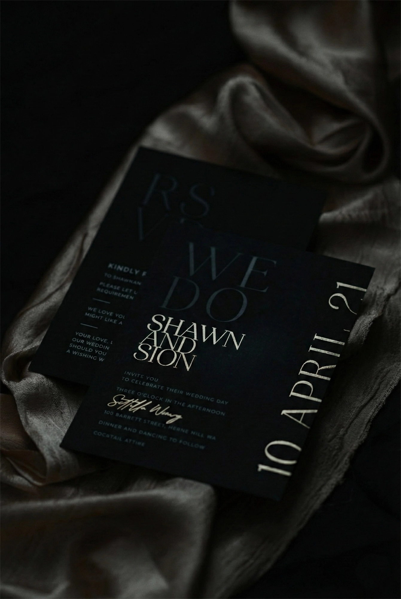 The Monaco wedding suite — Shawn and Sion black invitation with rose gold foil 'WE DO' typography and side date, RSVP card on draped silver silk
