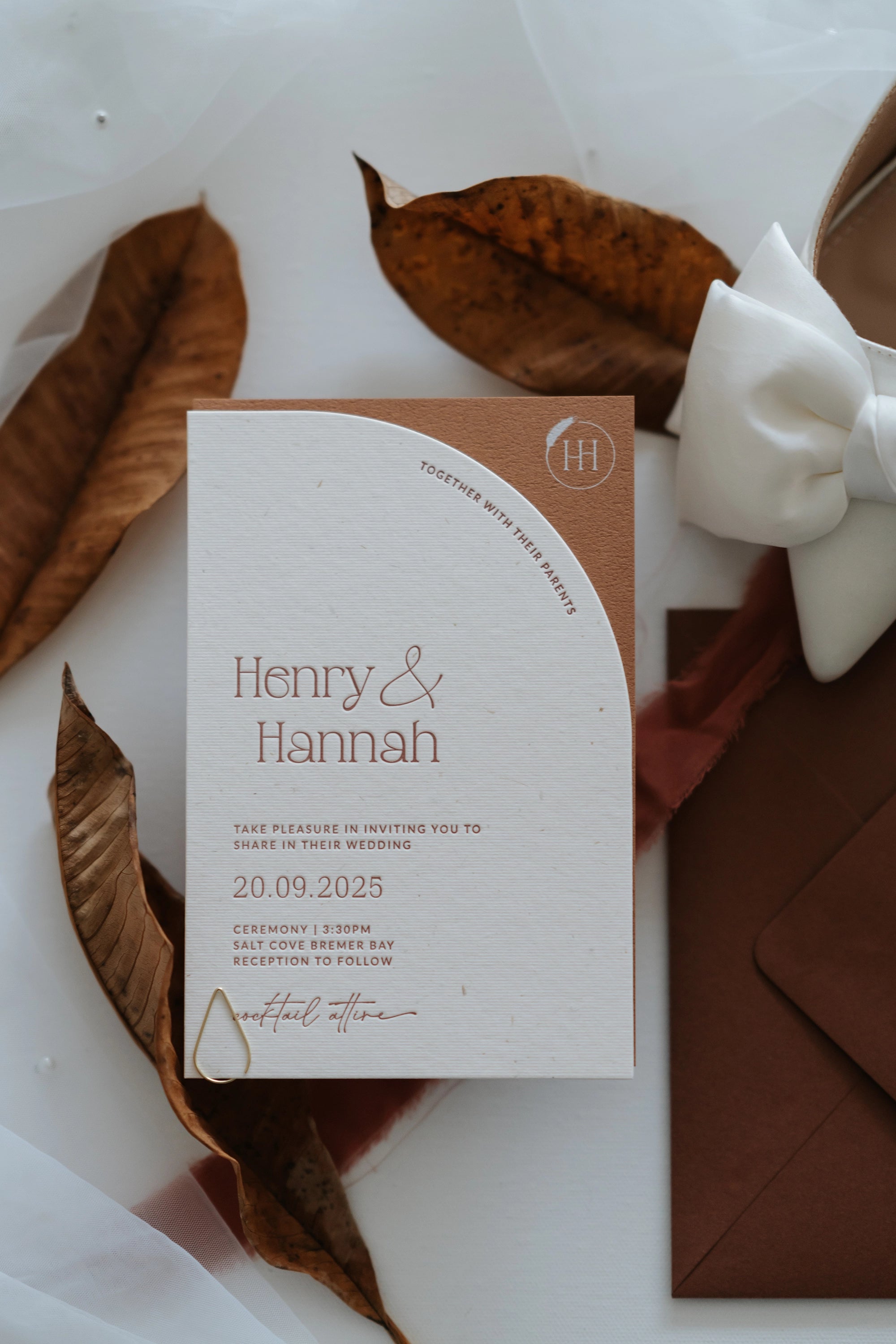 The Seville Suite arch invitation card on dried autumn leaves with terracotta envelope and white bow by Felicitations