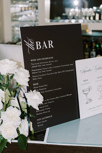 The Bar black wedding bar menu sign with signature cocktails card and white roses at wedding reception by Felicitations