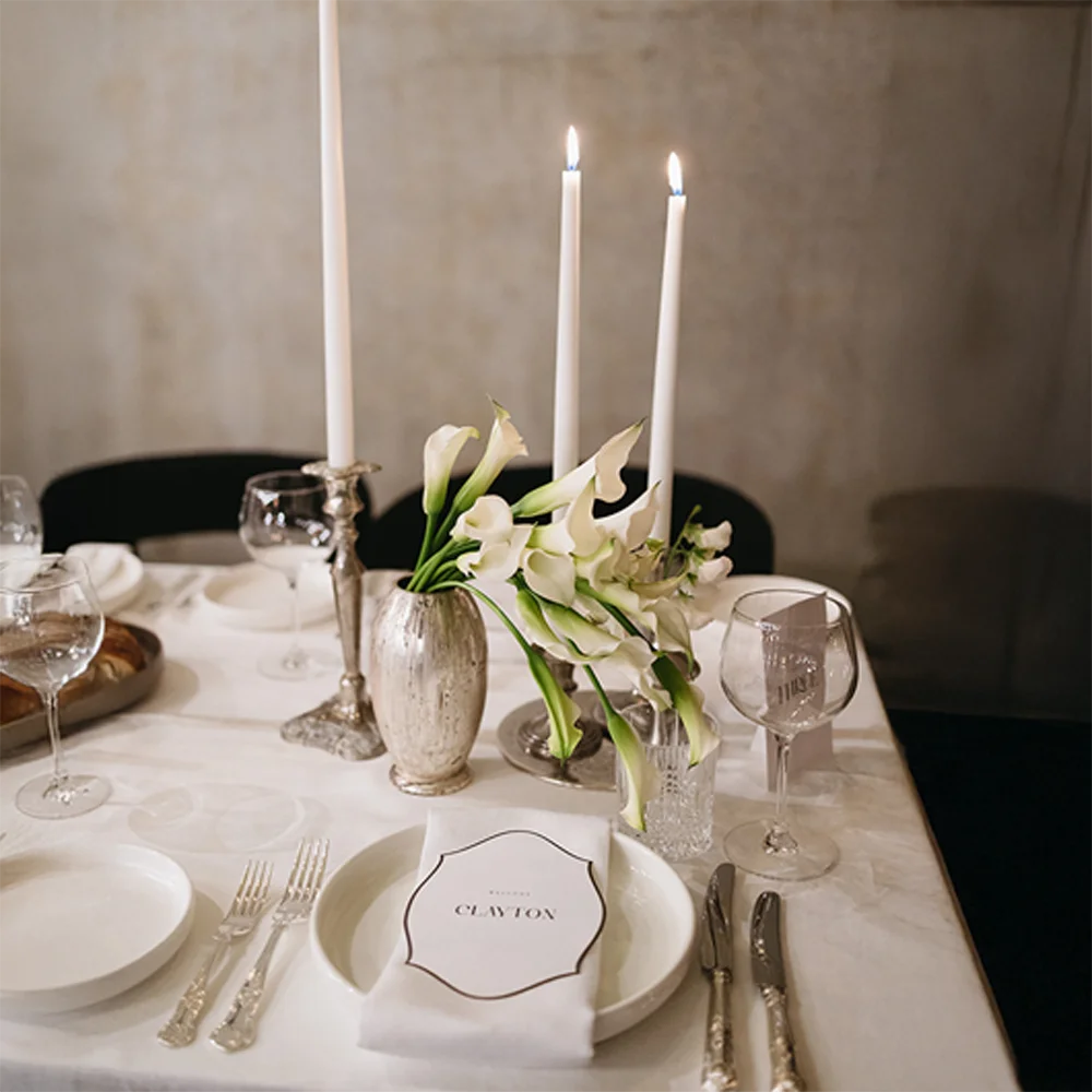 Elegant wedding menu and place card set for guest 'Clayton' by Felicitations Perth, styled with calla lilies, silver cutlery, and tapered candles on a white table setting.