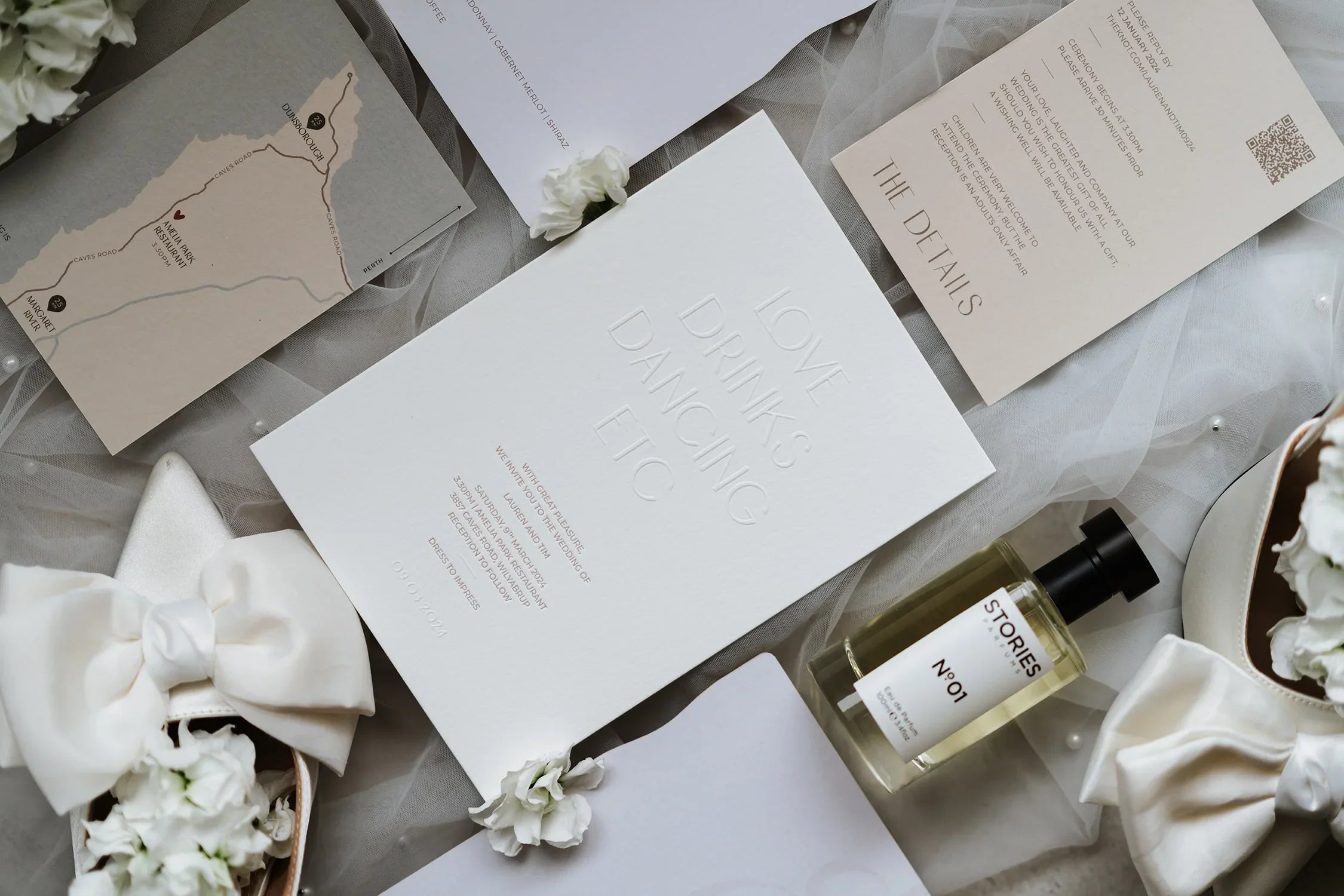 Elegant wedding invitation suite with white shoes, perfume, and floral accents on soft tulle