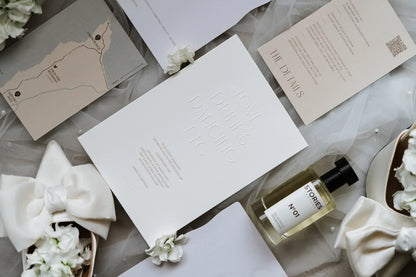 Elegant wedding invitation suite with white shoes, perfume, and floral accents on soft tulle