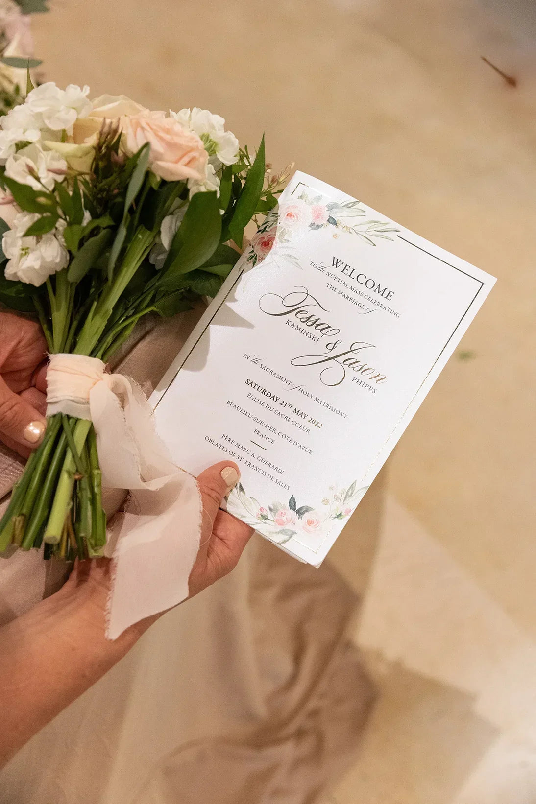 Hand holding wedding bouquet and floral wedding ceremony program with elegant script
