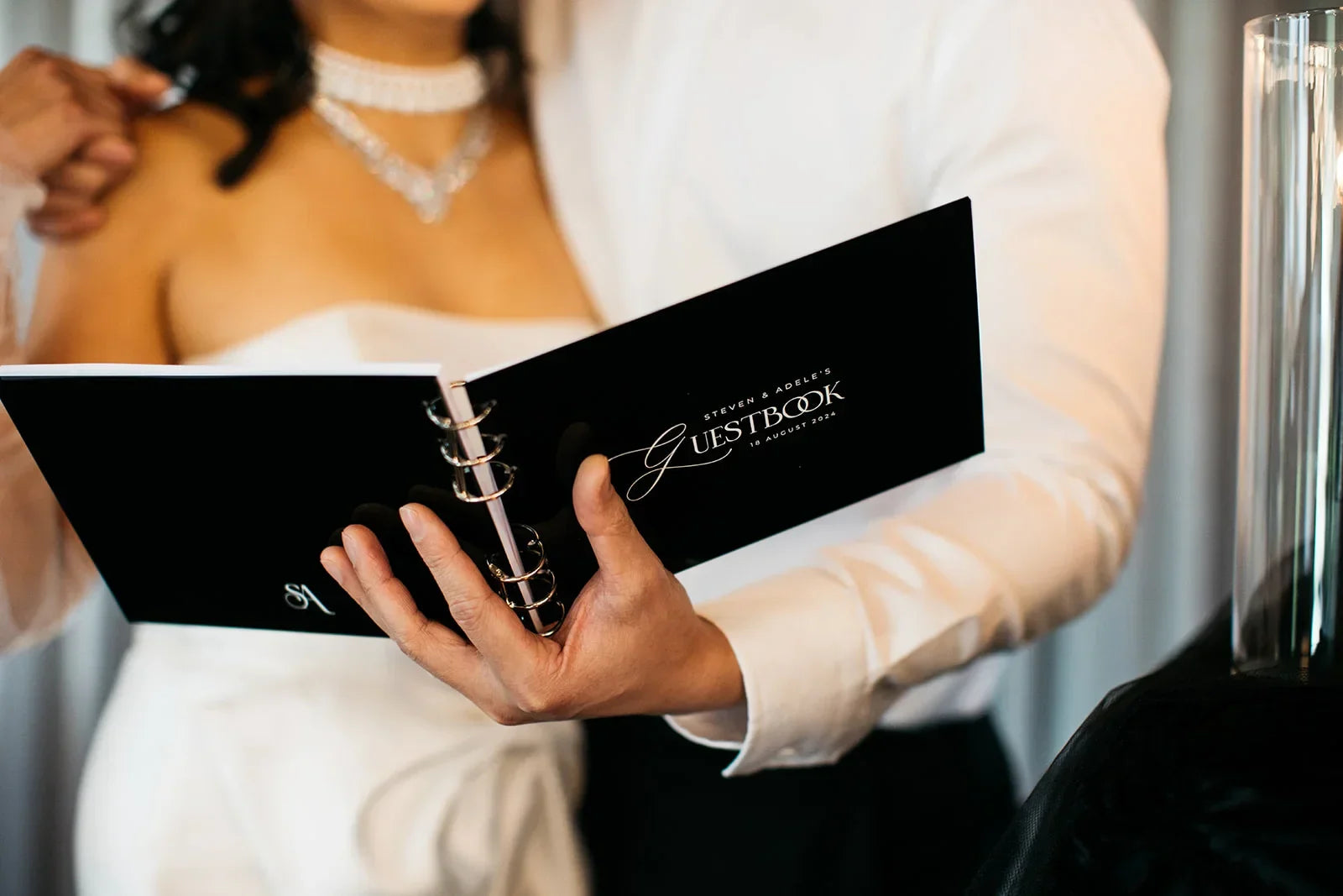 Bride and groom holding a black wedding guestbook in elegant white attire