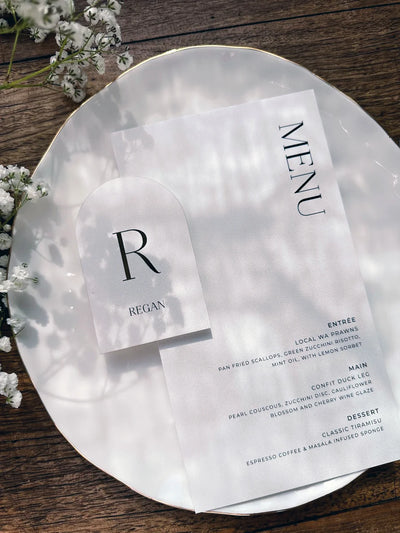 Vellum wedding menu and arch-shaped monogram place card for Regan styled on gold-rim glass plate with baby's breath