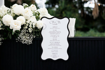 Black-bordered wavy-edge wedding bar menu 'Cin Cin All'Amore' with full drinks list, styled with lush white roses and chrysanthemums