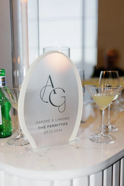 Frosted acrylic egg-shaped wedding bar sign 'Amore E Limone The Ferrittos' with AG monogram on marble bar with martini glasses