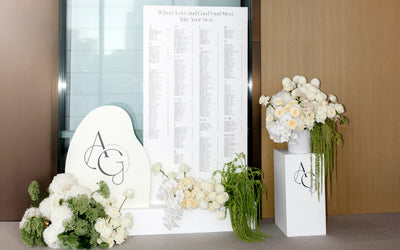 Modern wedding seating chart 'Where Love and Good Food Meet' with AG monogram cloud-shape and white floral arrangements at ceremony entrance