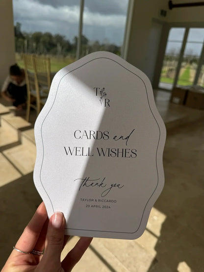 Hand holding elegant wedding card signage reading Cards and Well Wishes, Taylor & Riccardo, 20 April 2024
