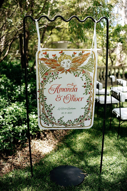 Hand-painted wedding sign for Amanda & Oliver with cherub and floral vine design outdoors