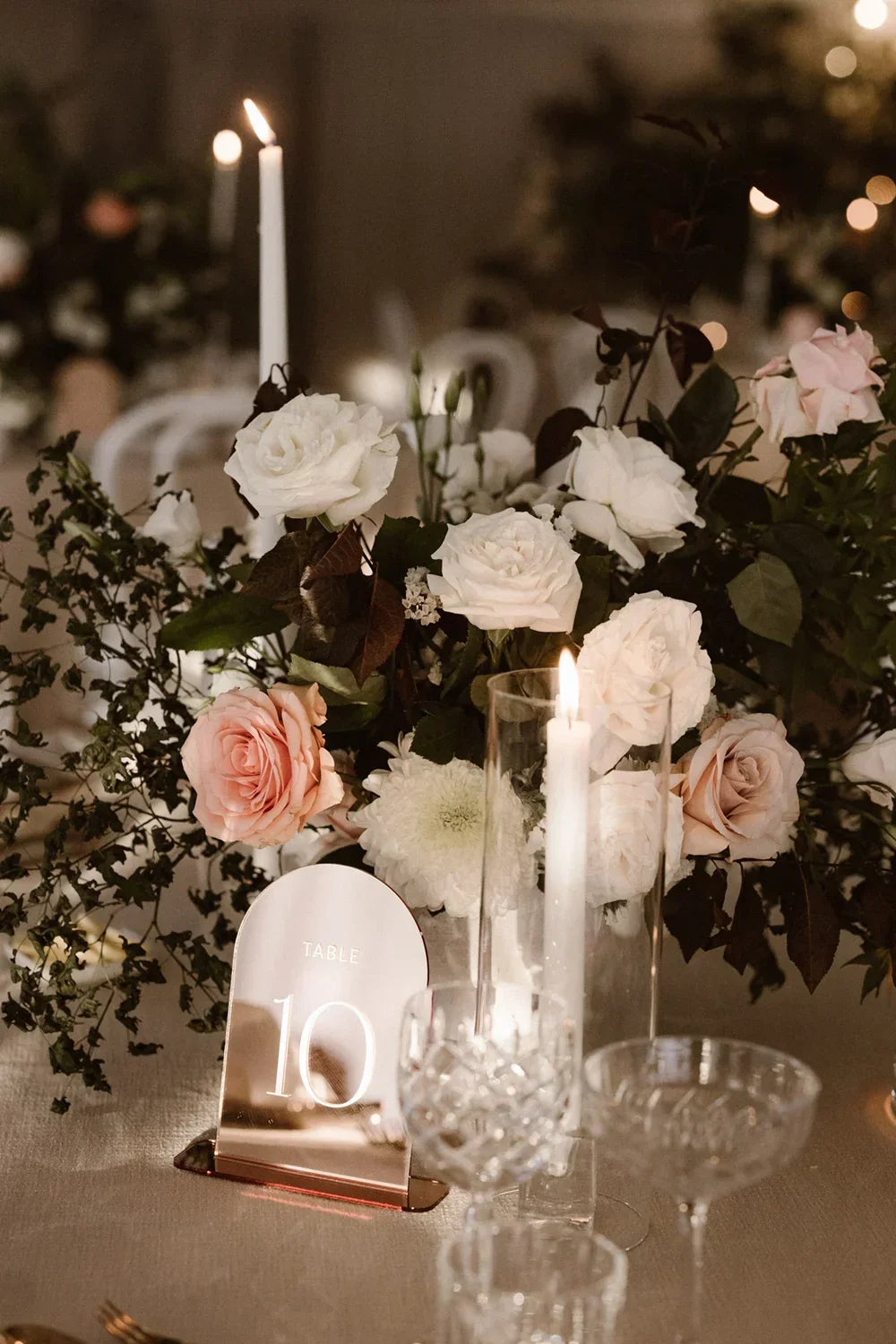 Elegant wedding table centerpiece with white and blush roses, lit candles, and rose gold table number 10
