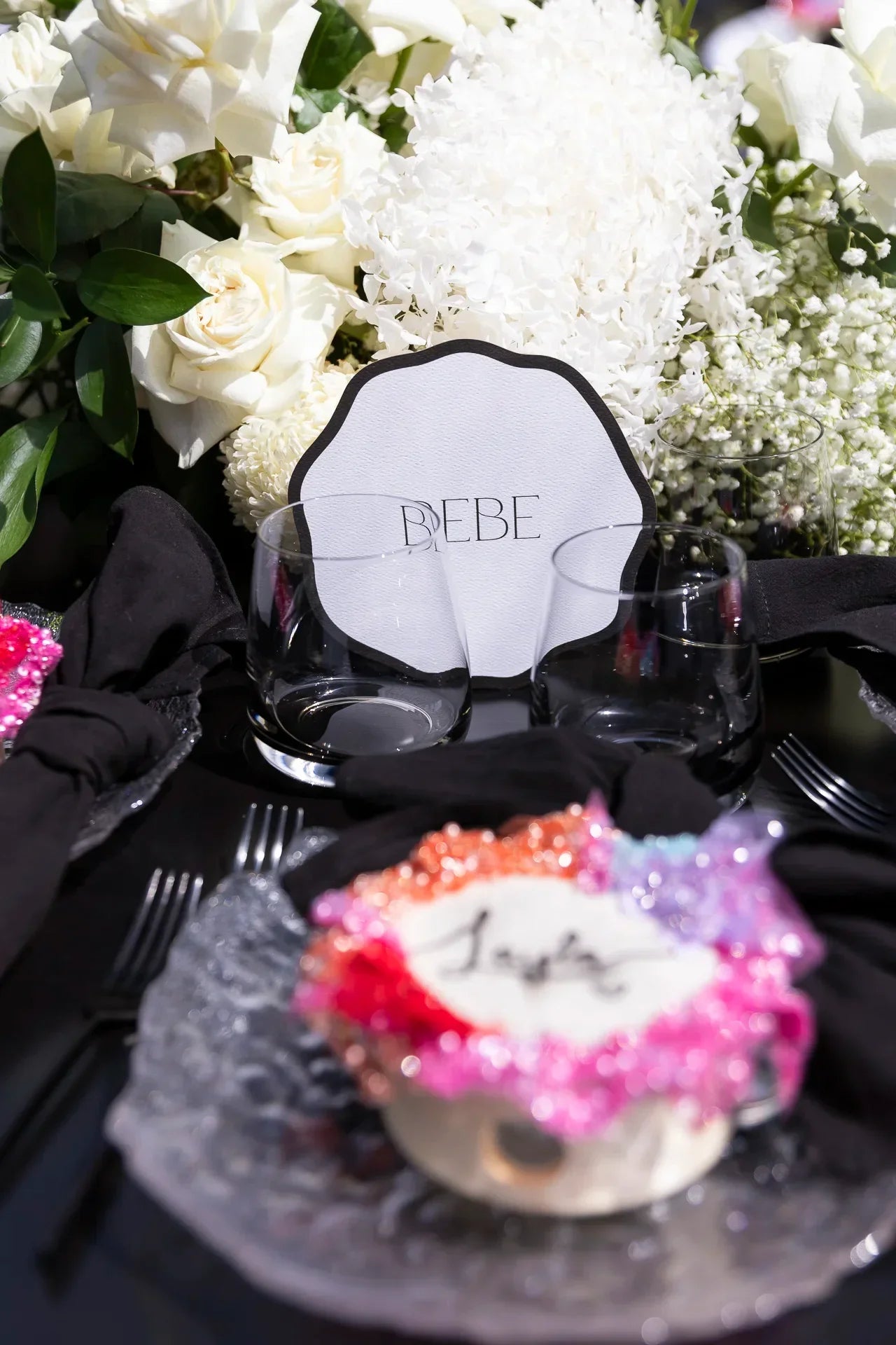 Elegant wedding table setting with white floral centerpiece, black napkins, and a card labeled Bebe
