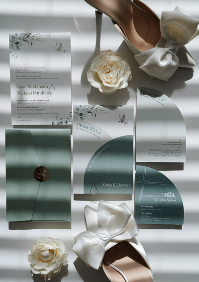 The Garda Suite wedding invitation flat lay with sage RSVP arch card map card and white satin bow heels by Felicitations