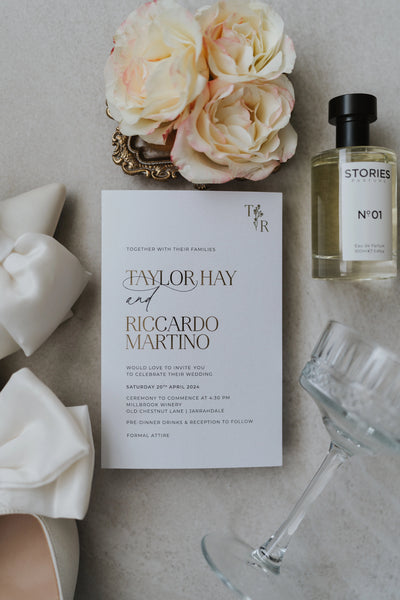 The Paris wedding suite — Taylor Hay and Riccardo Martino invitation with elegant gold foil typography and TR monogram, styled with cream roses and Stories perfume