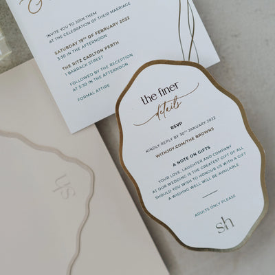 The Positano suite details card close-up — gold foil edge on cloud-shaped RSVP and gifts card with matching blush wavy envelope debossed monogram
