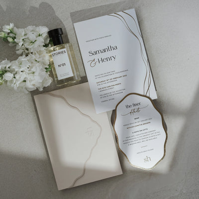 The Positano wedding suite — Samantha and Henry invitation with gold foil flowing line motif, scallop-edged details card and blush wavy envelope flat-lay with white florals