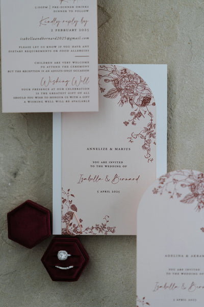 The Lisbon suite details flat-lay — wishing well card and burgundy floral arch invitation with hexagonal velvet ring box and diamond engagement ring