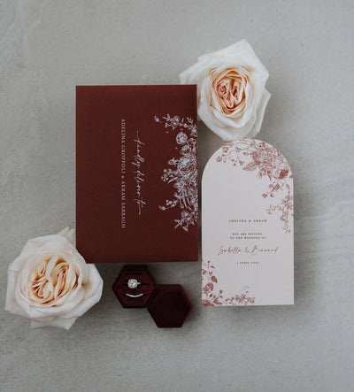 The Lisbon wedding suite flat-lay with burgundy printed envelope, blush arch invitation and cream roses with hexagonal velvet ring box