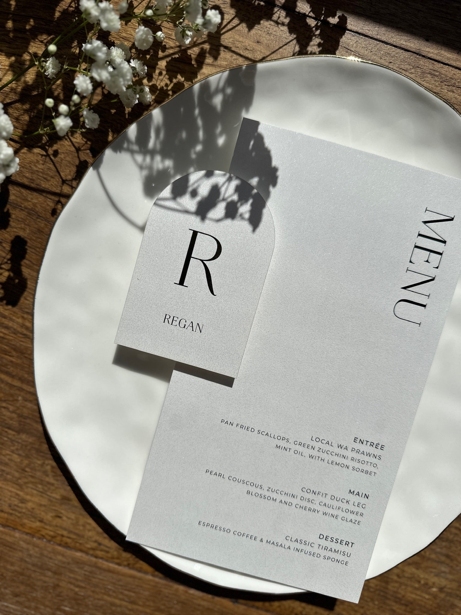 The Santorini Suite shimmer arch menu card and Regan place card with monogram on white plate by Felicitations Wedding Stationery